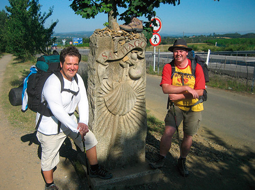 Die Alpensterne mit Rucksäcken an einem Wegstein mit Jakobsmuschel und der Aufschrift „Santiago“